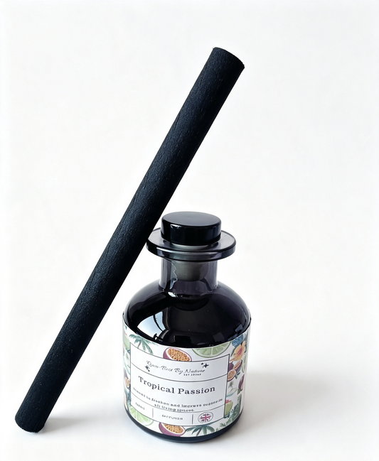 A reed diffuser bottle with a black glass body and matching black cap, next to a long black reed stick. The bottle has a decorative label reading 'Tropical Passion' with botanical illustrations.