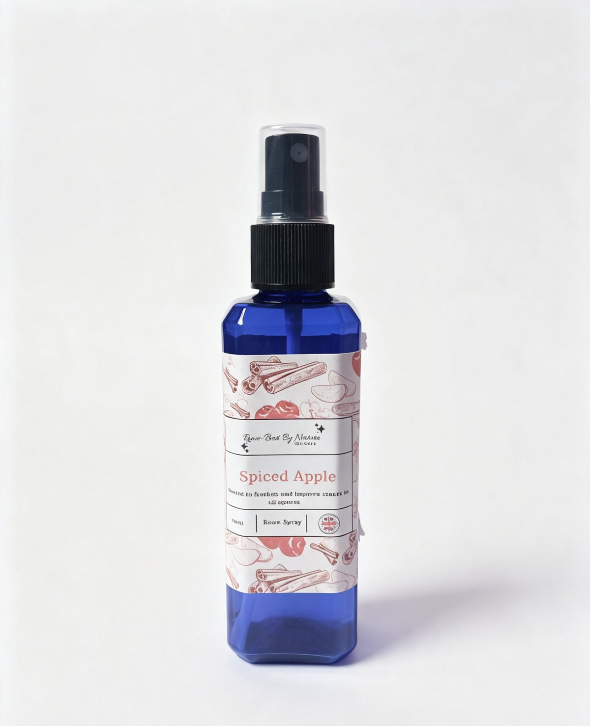 A blue spray bottle with a black pump dispenser and a white label featuring red and pink illustrations of cinnamon sticks and a red apple. The label reads 'Spiced Apple' and the brand Rowe-best by nature