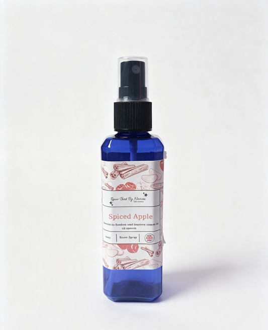 A blue spray bottle with a black pump dispenser and a white label featuring red and pink illustrations of cinnamon sticks and a red apple. The label reads 'Spiced Apple' and the brand Rowe-best by nature